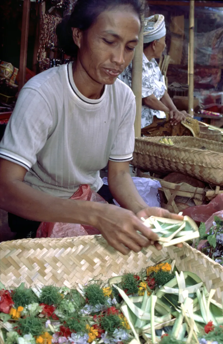 A woman makes offerings to sale in the Ubud market.
Balinese people make such offerings out of palm leaves, flowers, and incense for use in everyday rituals intended to appease supernatural forces.