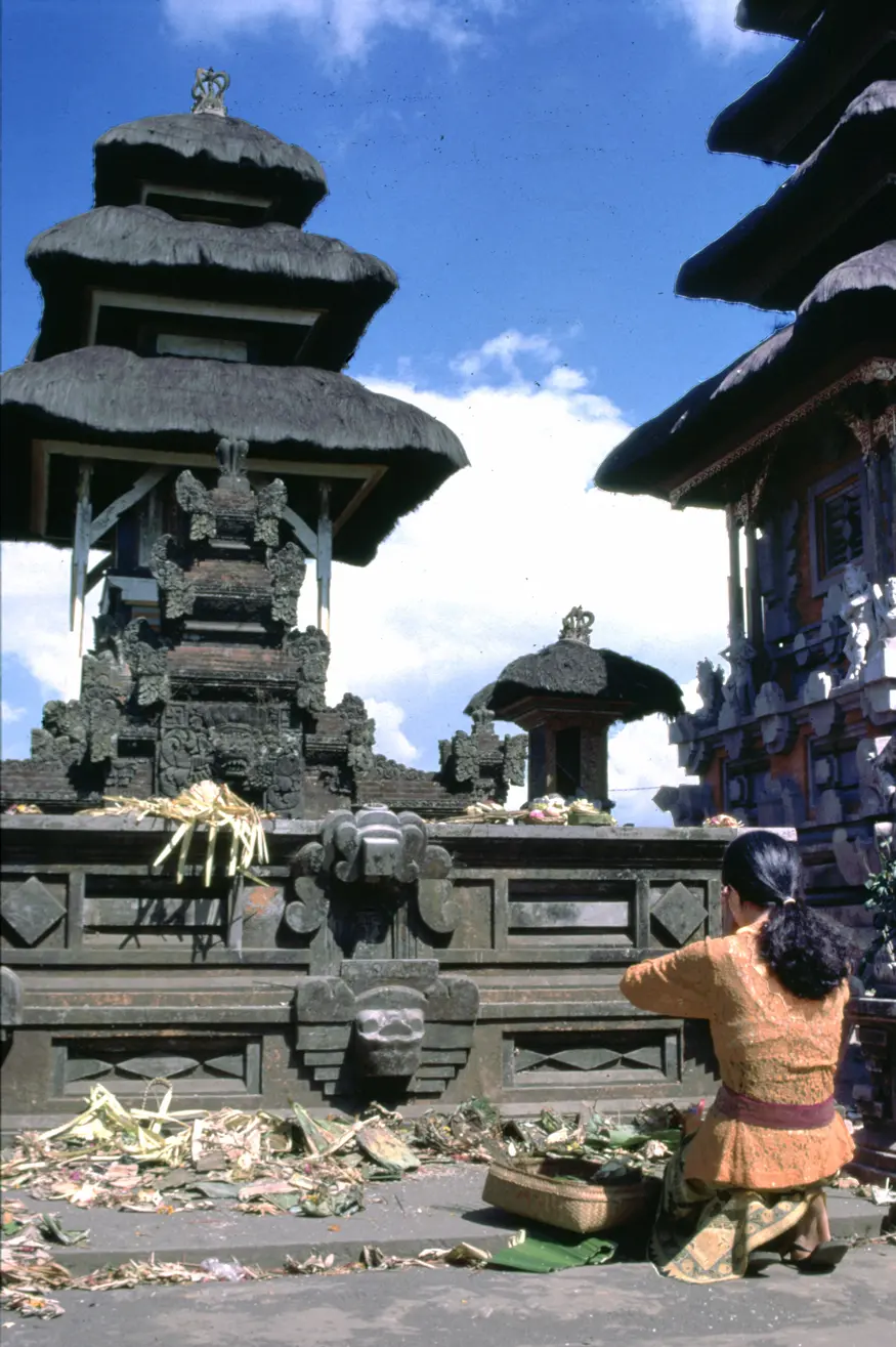 A woman places an offering on the altar of the Kintamani Ulan Dano Hindu temple in Bali. Old offerings cover the altar and the ground surrounding it.