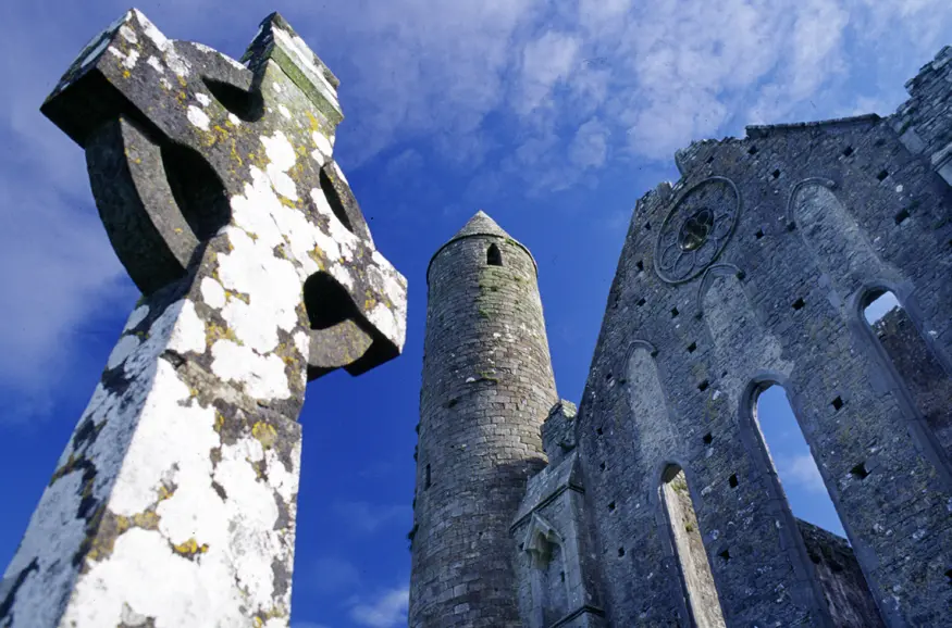 A Celtic cross sits in front of a 700 year old gothic cathedral on the Rock of Cashel. Other medieval stone buildings share the view from the Rock, rising high off the surrounding plains on this solitary hill.