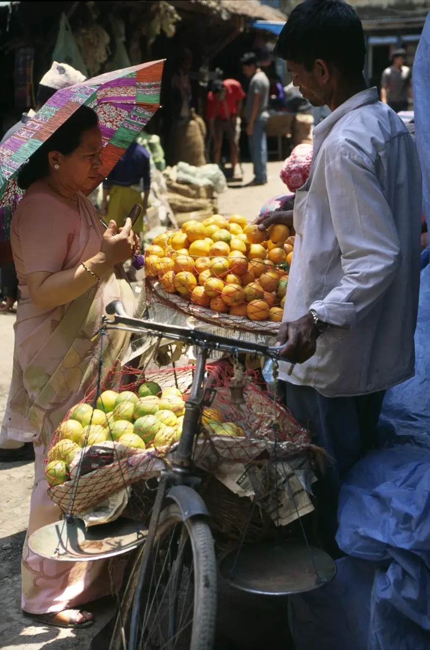 A woman buys oranges from a vender who carts his goods around on his bicycle.