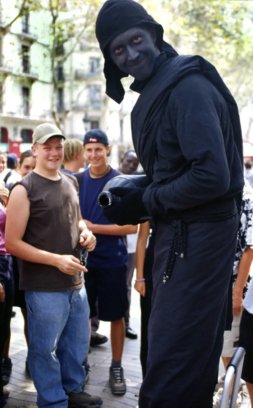 The tree-lined pedestrian area of Barcelona's La Rambla attracts tourists, locals, and street performers such as this human statue. This black bandit stands still until offered a coin, then he turns into a fountain, pouring mysterious liquid into an oil pan below his feet.