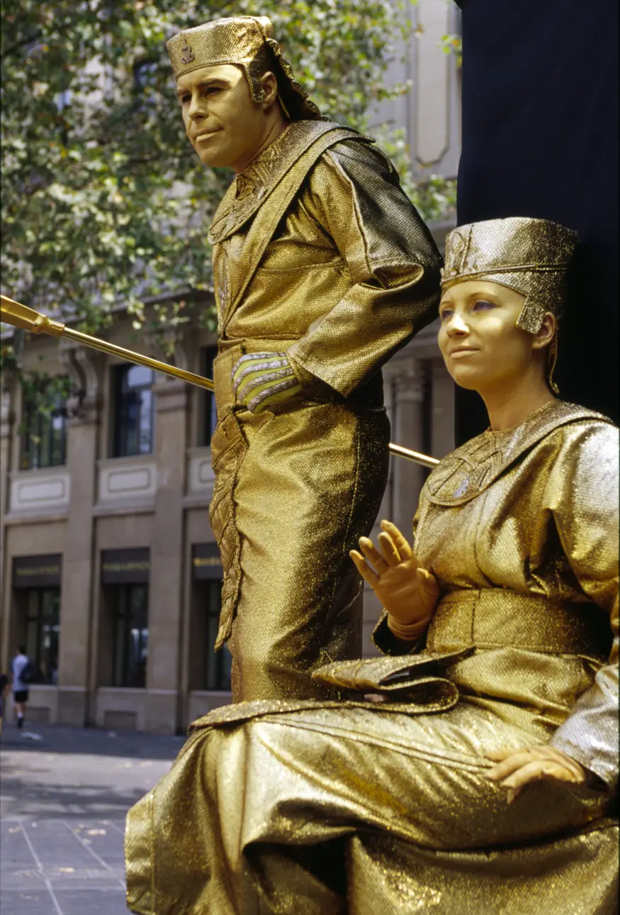 The tree-lined pedestrian area of Barcelona's La Rambla attracts tourists, locals, and street performers such as these human statues. This gold couple stands still until offered a coin, then they move slowly into position for photographs with the kids.
